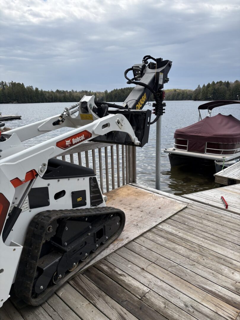 Bobcat loader on dock beside covered pontoon boat