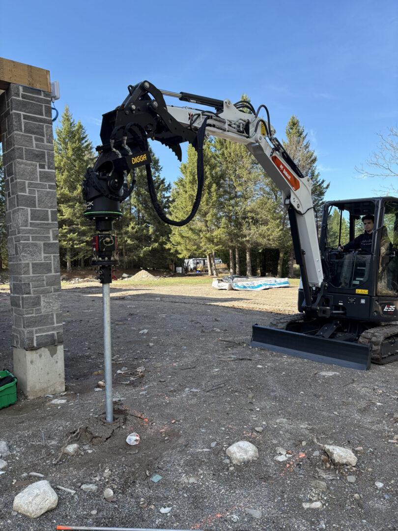 Mini excavator drilling post beside stone pillar
